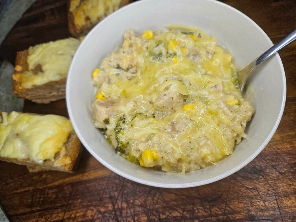 Creamy Chicken noodle soup served in a bowl on a cutting board with garlic cheese bread.