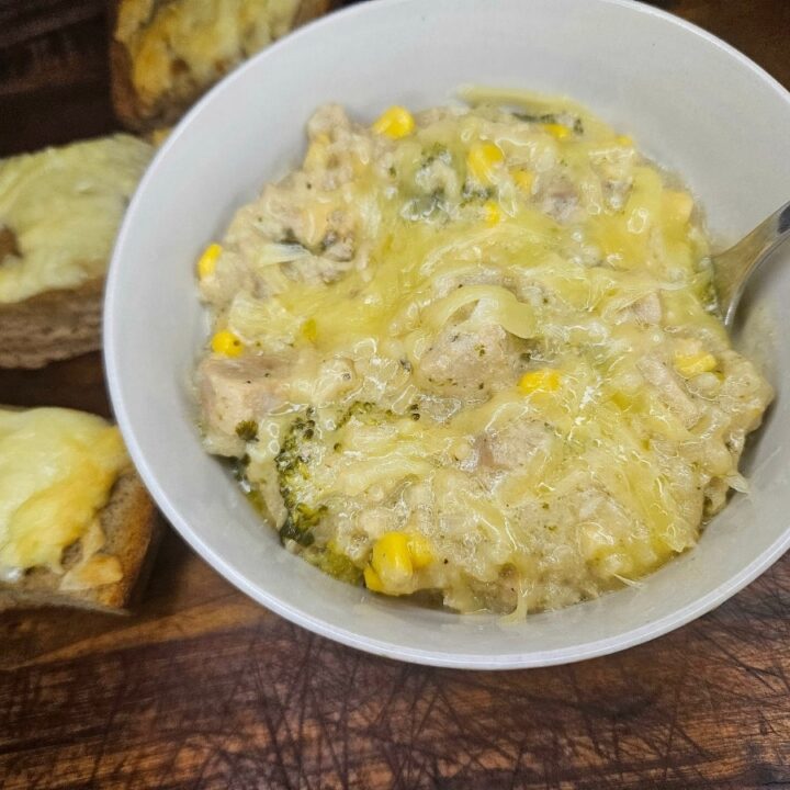 Creamy Chicken noodle soup served in a bowl on a cutting board with garlic cheese bread.