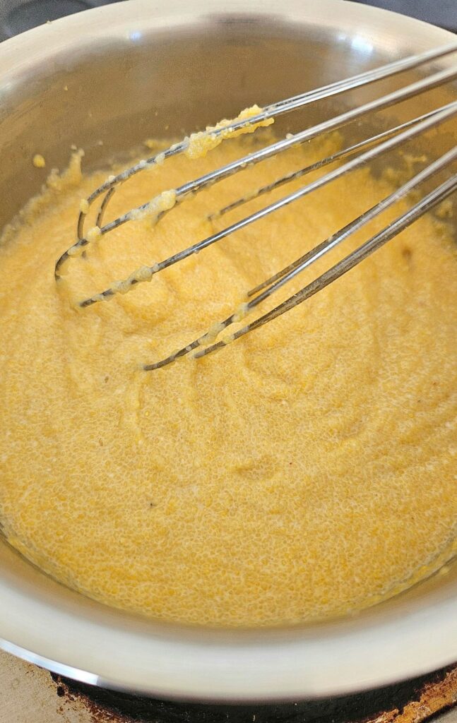 Stirring creamy polenta in a stainless steel pot.
