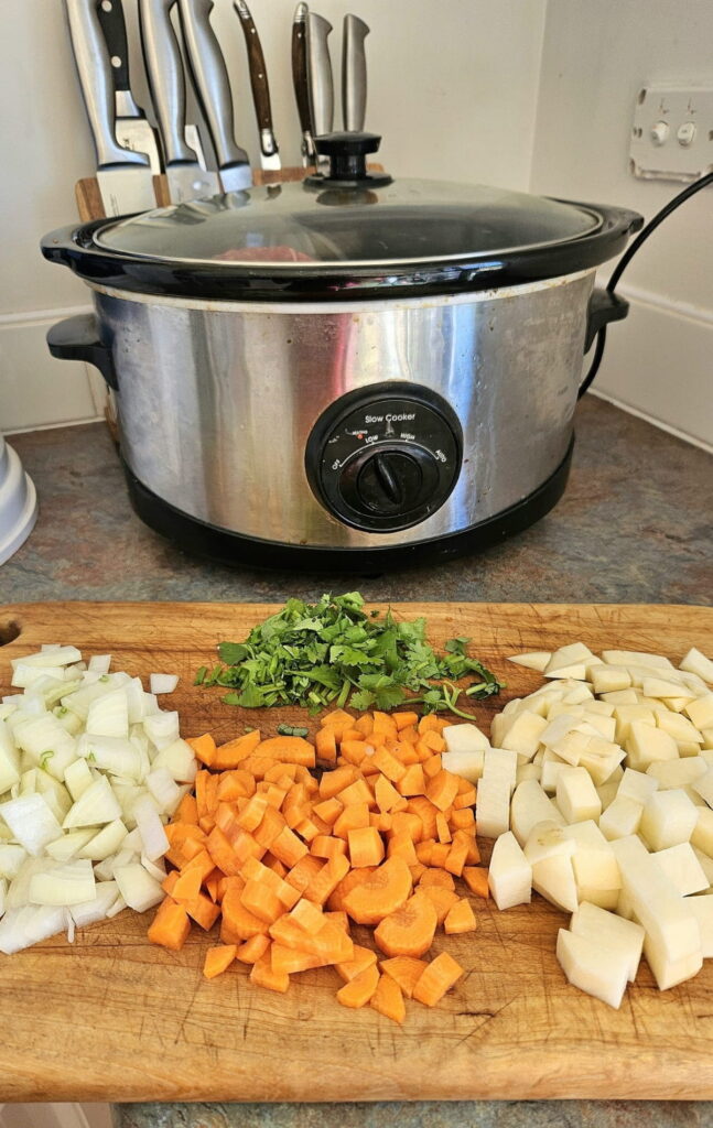 Beef stew ingredients on a cutting board with slow cooker in background.