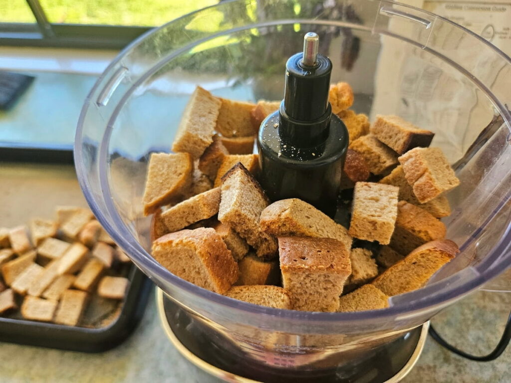 Bread pieces in a food processor waiting to be pulsed into breadcrumb.