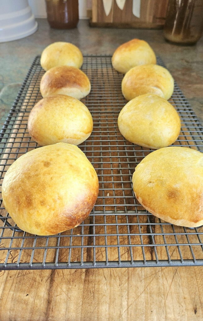 Sourdough hamburger buns resting on a cooling rack.