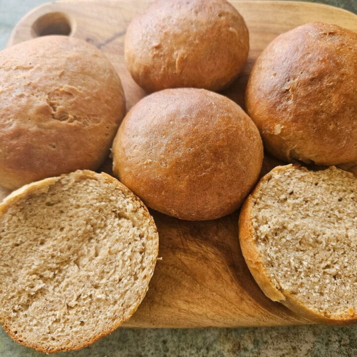 Hamburger buns on a cutting board. One cut open.