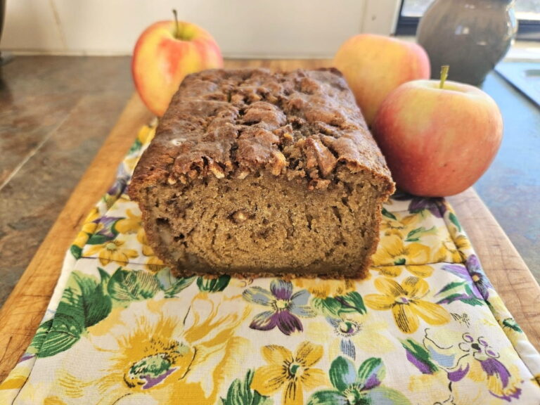 Sourdough apple bread resting on a cutting board surrounded by apples.