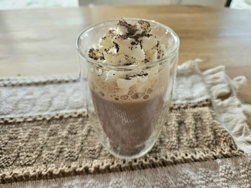 Chocolate milk in a glass cup topped with whip cream.