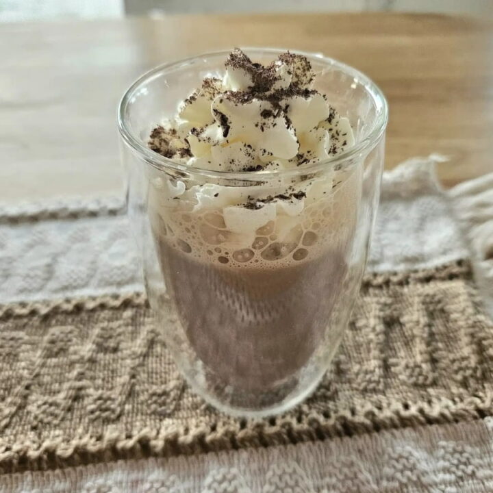 Chocolate milk in a glass cup topped with whip cream.