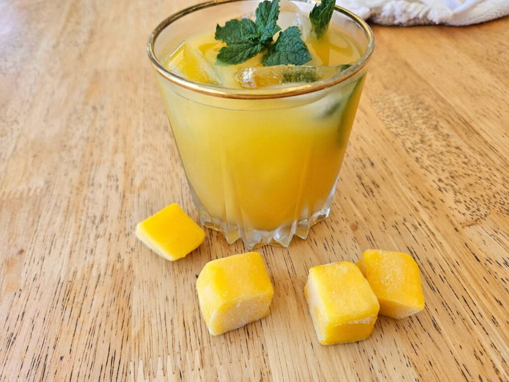 Mango iced tea with peppermint leaves in a glass cup on the table.