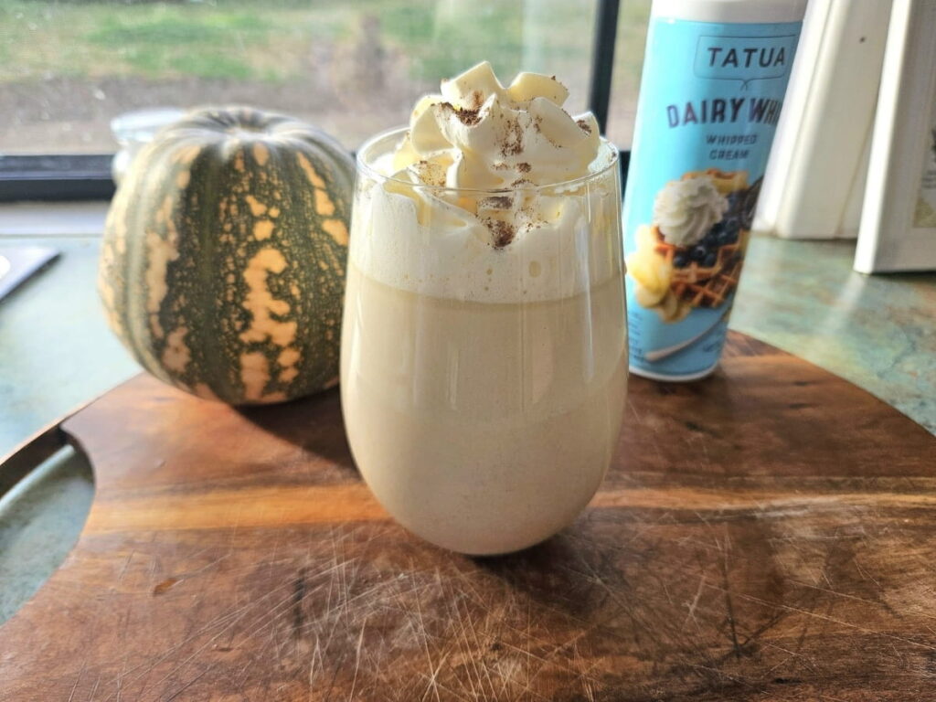 Pumpkin latte in a glass cup on a cutting board with whip cream.