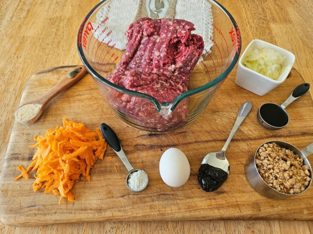 Rissole ingredients on a cutting board. Mince, eggs, salt, sea salt, grated onion and grated carrot.