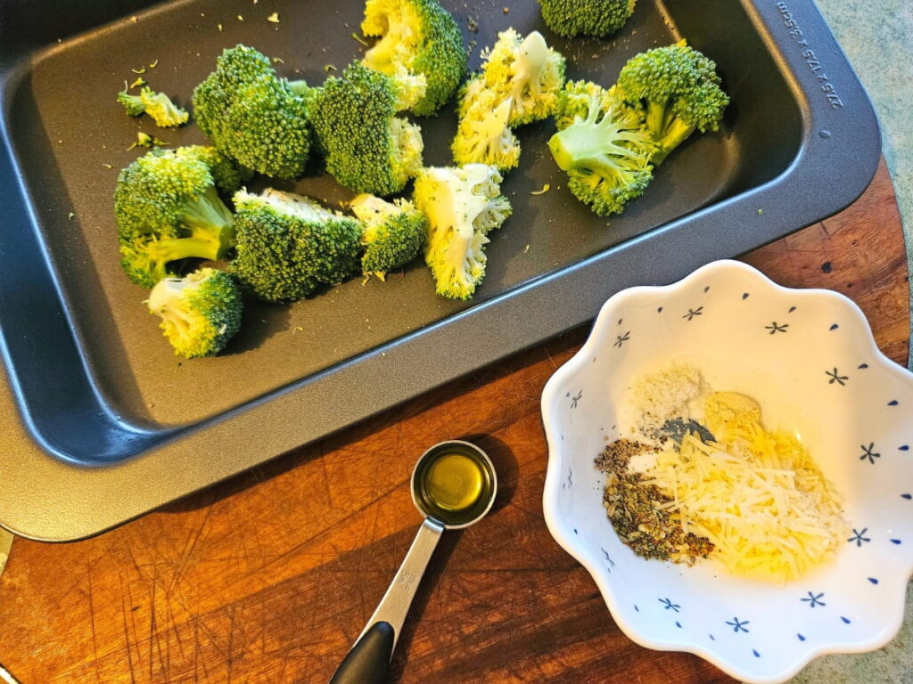 Chopped broccoli in a tray with spices in a bowl.