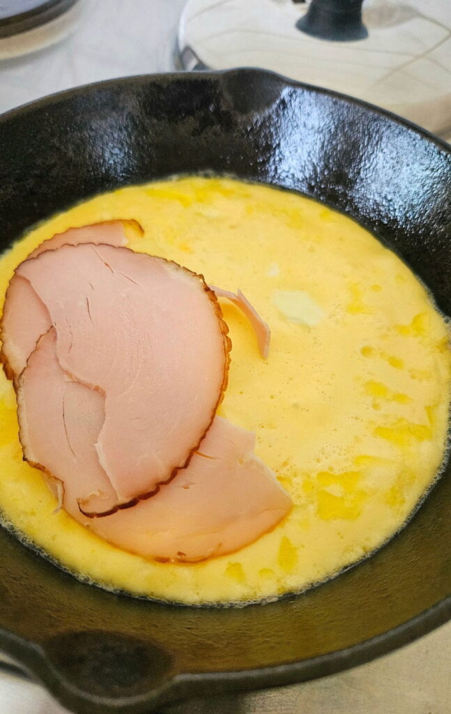 Cooking an omelette with turkey and cheese in cast iron pan.